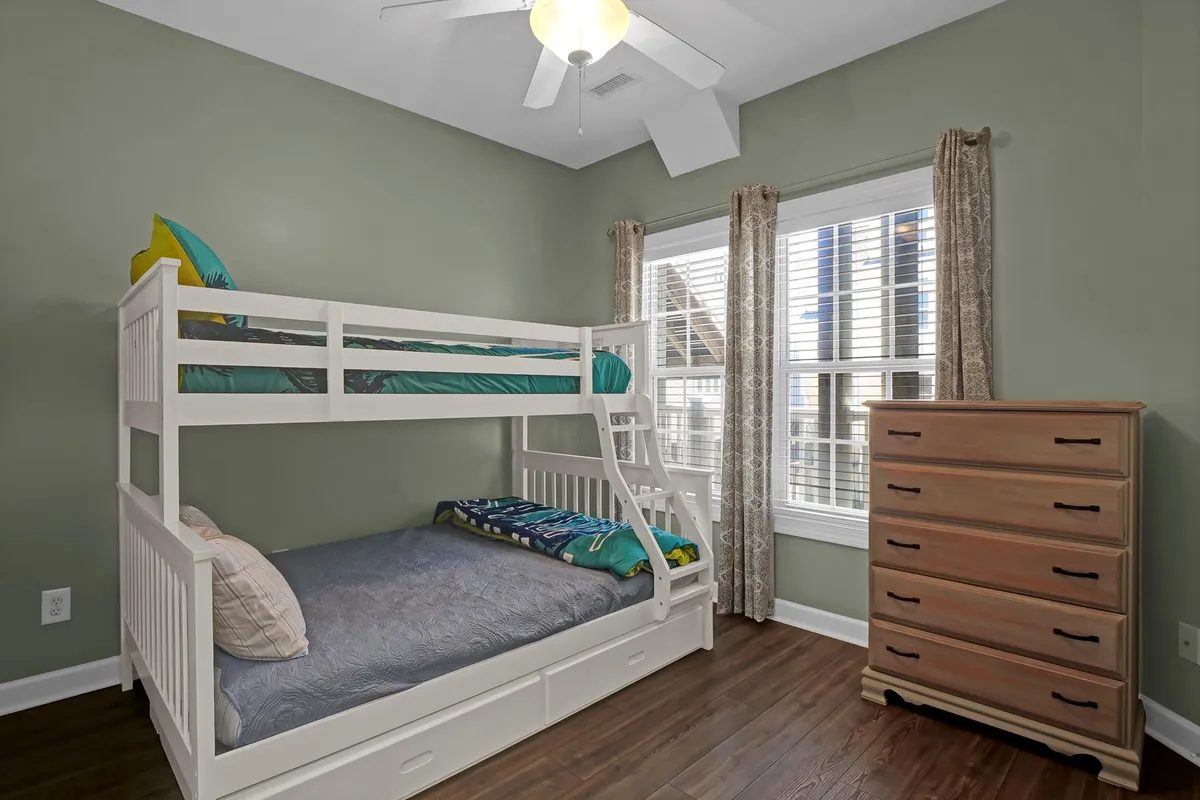 A cheerful second bedroom featuring a sturdy twin-over-full bunk bed, a trundle bed beneath, and bright sunlight streaming in through the window. The décor is playful yet comfortable, appealing to families and friend groups alike.