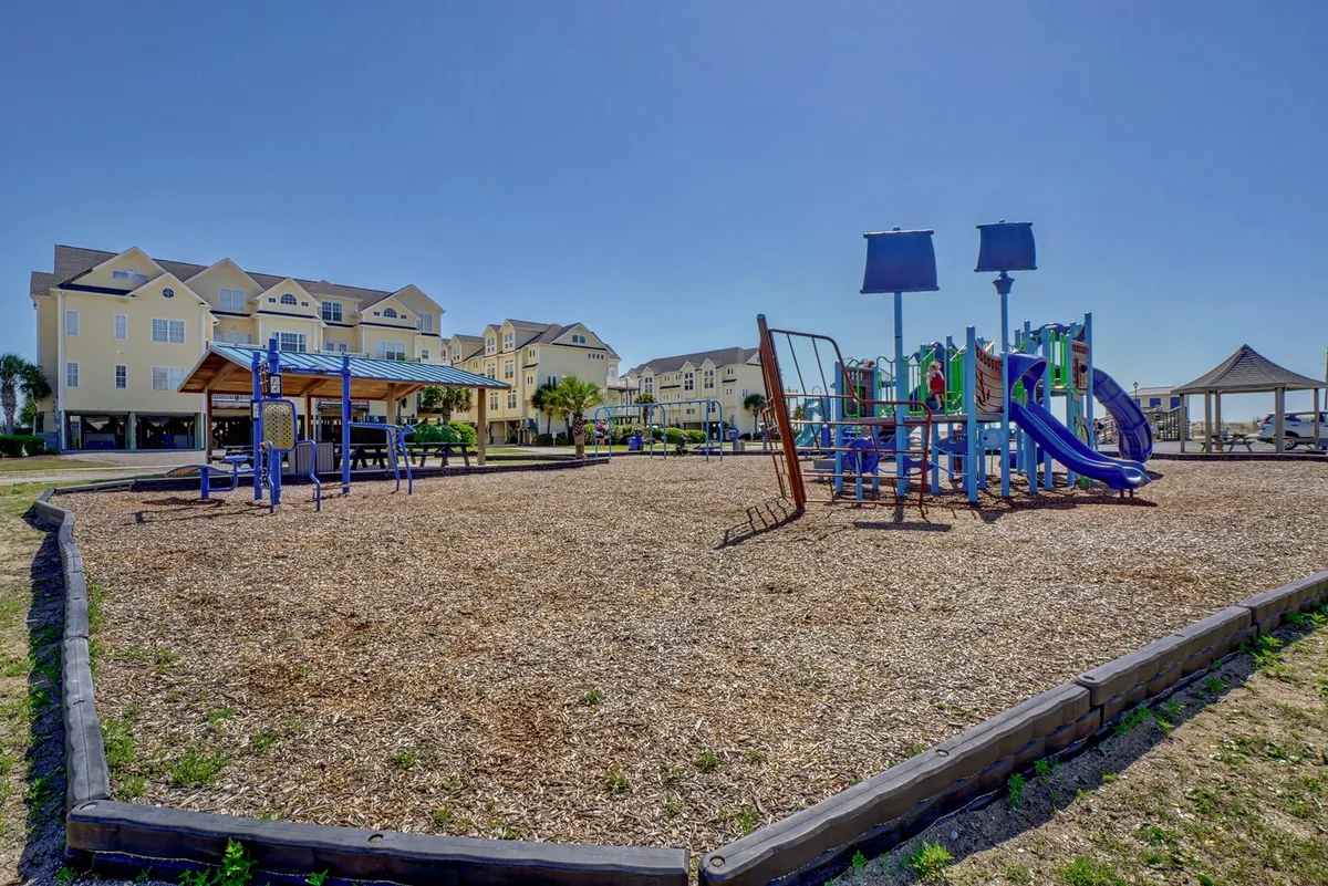 A vibrant playground with colorful equipment and an adjacent open space, set beside a residential building. The area is lively and welcoming, perfect for children and community gatherings.