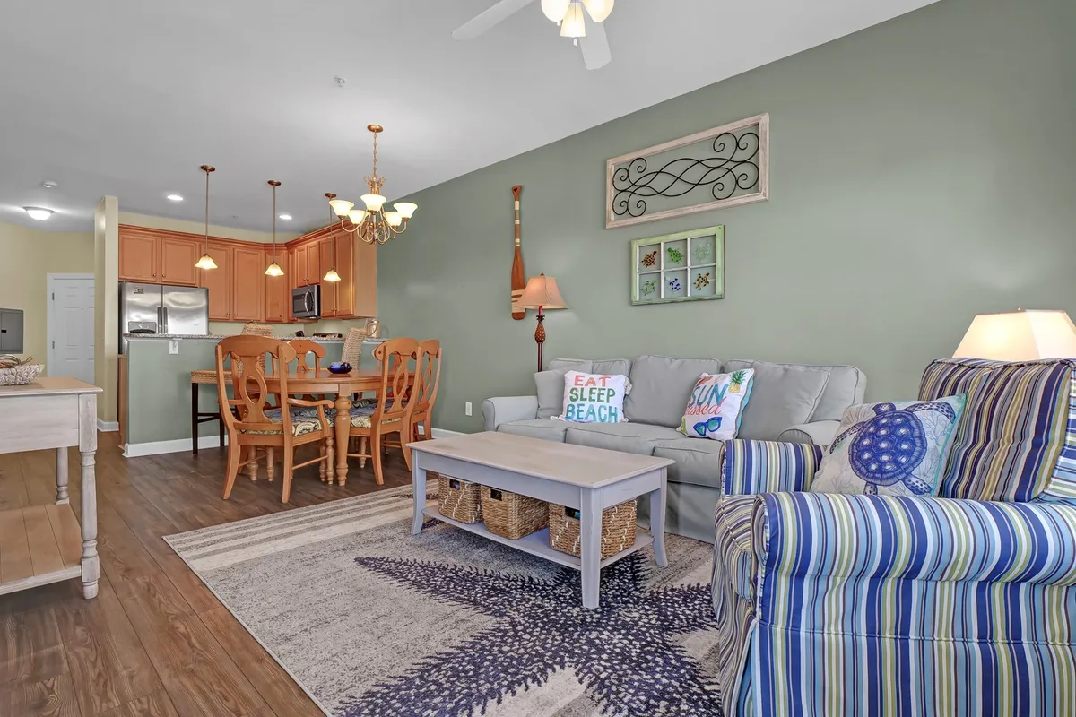 This image presents a bright and cheerful open-concept living and dining space. The focal points include a comfortable sofa, a dining table perfect for meals or games, colorful cushions, decorative wall art, and a cozy rug. Natural light pours in through large windows, creating an inviting and vibrant atmosphere.