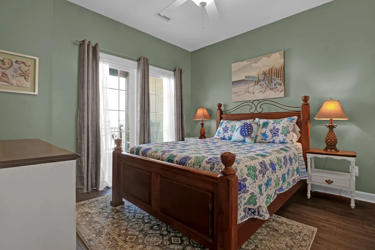 A tranquil bedroom with a plush bed adorned in colorful bedding, a nightstand with a lamp, artwork on the wall, and soft curtains framing windows that let in natural light. The overall atmosphere is peaceful and restful, embodying the sense of a personal sanctuary.