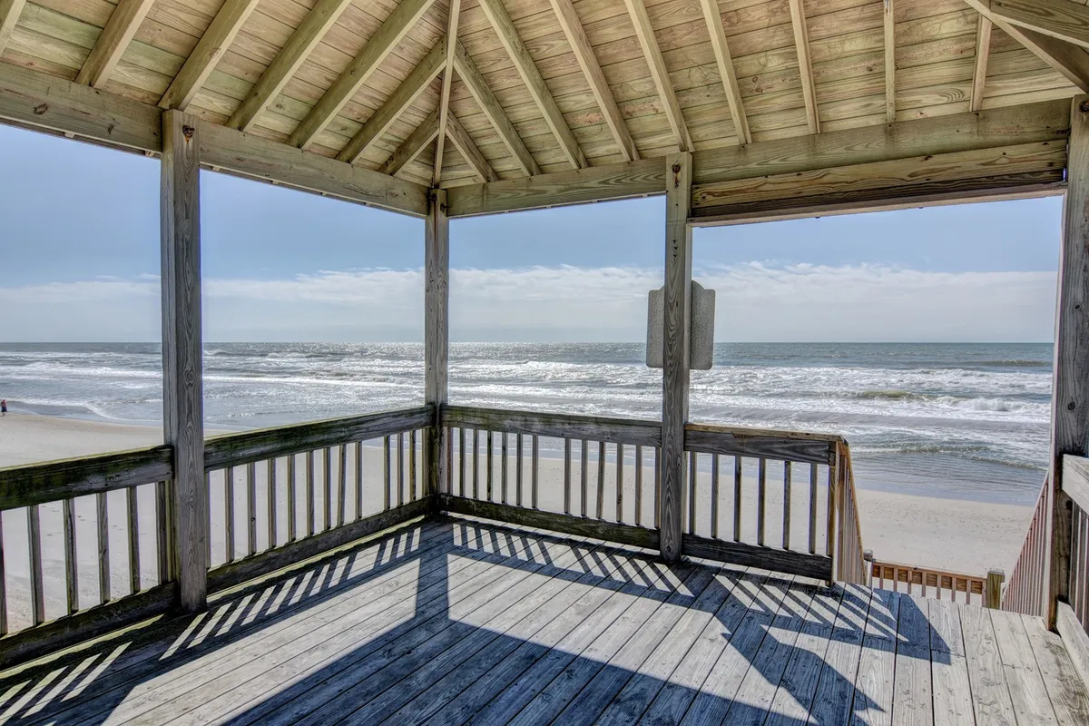 A spacious wooden deck with an open pavilion structure overlooking an unobstructed ocean view. The seating area suggests a welcoming spot to unwind, enjoy the breeze, and relax after a day of adventure, with space for your pet to lounge nearby.