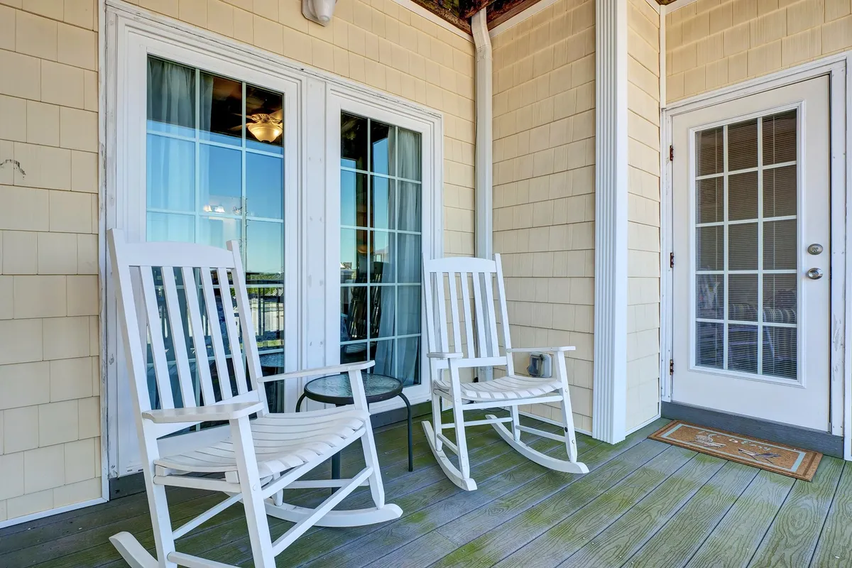 A peaceful wooden deck furnished with classic rocking chairs and French doors opening to the home. The deck is bathed in soft, natural light, hinting at gentle breezes and the sound of the ocean nearby. It offers a tranquil spot perfect for morning coffee or relaxing as the day winds down.