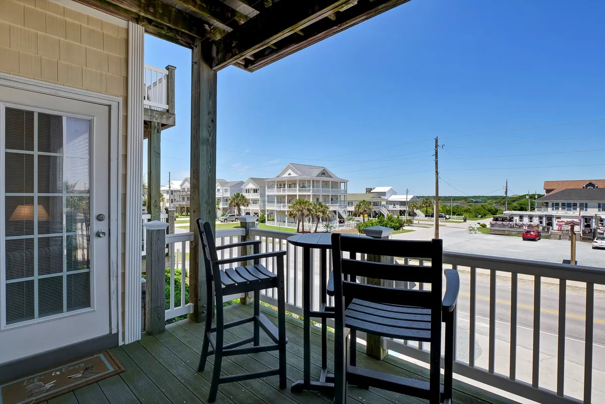 An exterior shot showcasing comfortable balcony seating with a view of neighboring houses and the scenic landscape. The inviting setting is ideal for gathering with friends and enjoying the evening ambiance, suggesting an ideal base for sociable nights before heading out.