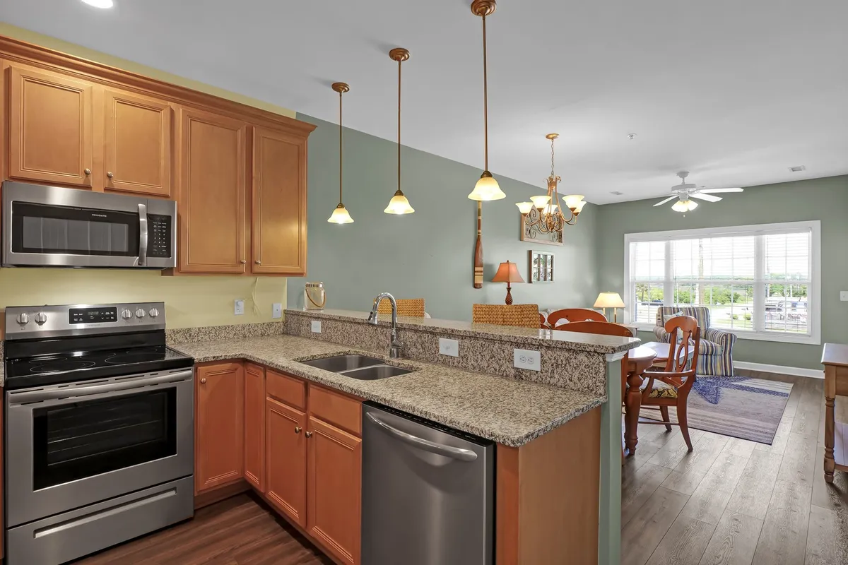 The photo reveals a modern, well-stocked kitchen with granite countertops, stainless steel appliances, pendant lights, and an adjacent dining area with a scenic window view. The setting is warm and welcoming, ideal for cooking and sharing family favorites.