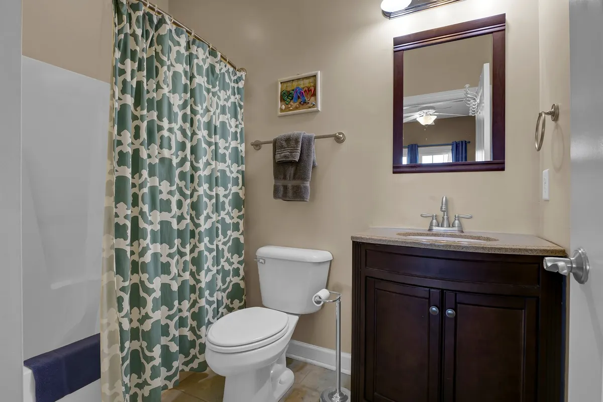 A cozy ensuite bathroom with a modern vanity, large mirror, and a shower curtain, offering a private space to refresh and unwind. The design is inviting and practical, supporting both morning routines and quiet moments.