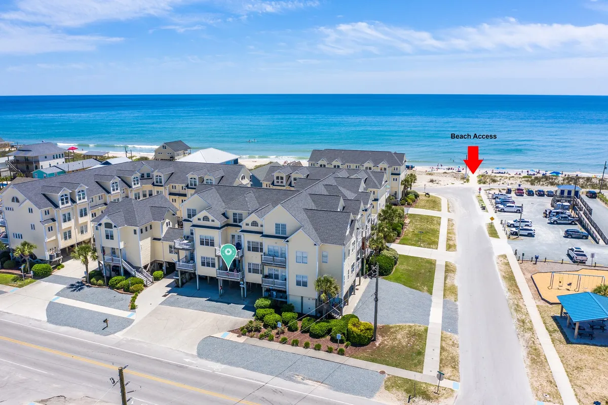 A vibrant exterior scene showing easy beach access, residential buildings, and a parking area, all steps from the sand. The area is open, inviting, and practical for families traveling with pets, offering direct routes for walks and outings.