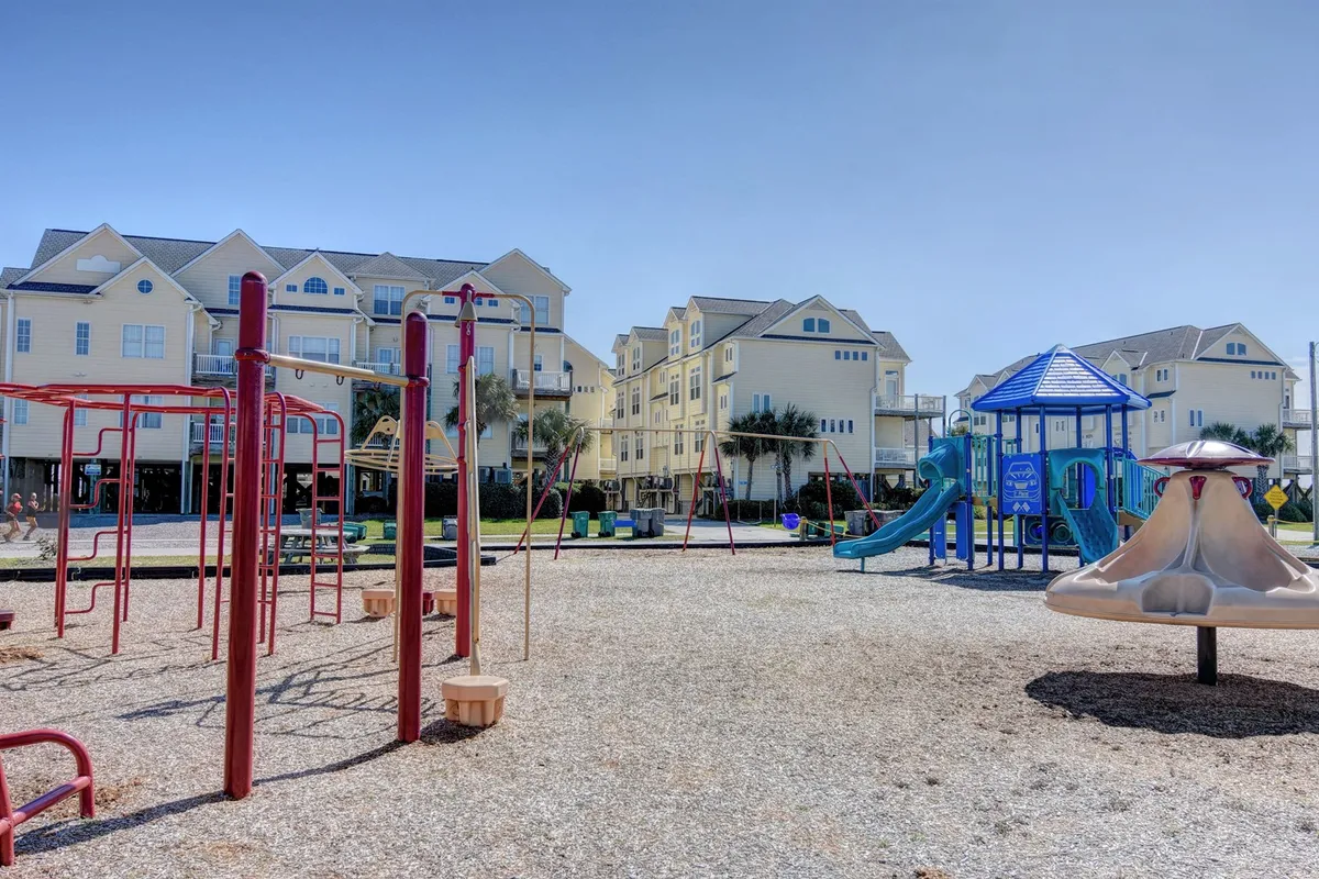 A colorful, modern playground filled with swings, slides, and a climbing structure. Children are actively playing, with family members nearby, surrounded by well-kept greenery. The joyful scene captures the spirit of kids burning off energy while parents relax close by.