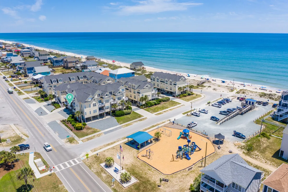 A joyful exterior scene featuring a beachfront playground, residential buildings, and a parking area. Families and children are engaged in playful activities, with the beach just beyond, capturing the lively, accessible, and family-friendly vibe of the area.